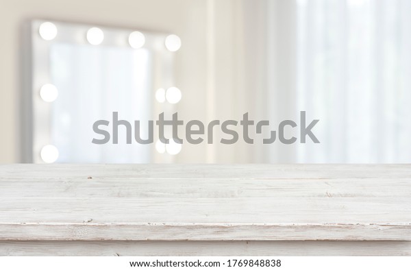 Defocused makeup mirror in dressing room with wooden\
table top