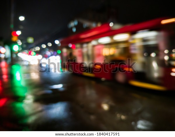 defocused night rain city street view with red bus\
crossing road