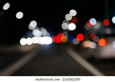 Defocused night street view from drivers perspective, with bokeh blur of street lights. Colorful night city life background.