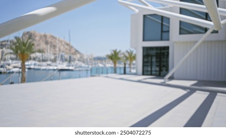 Defocused outdoor photo of modern architecture with a clear blue sky, palm trees, marina in the background, and foreground shadows. - Powered by Shutterstock