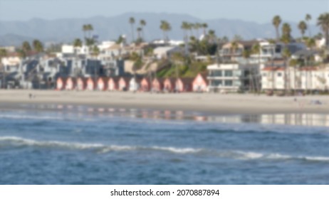 Defocused pacific ocean coast from pier. Sea water waves tide, shore sand. Beachfront vacations resort. Waterfront Oceanside, California USA. Tropical palms, cottages on beach. Reflection in littoral.
