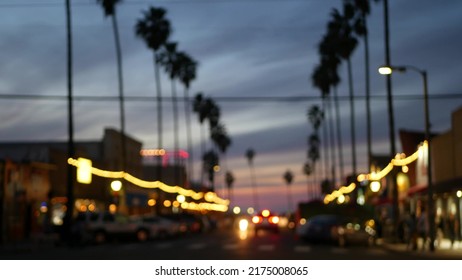 Defocused Palm Trees In Ocean Beach, Lights In Twilight, California Coast, San Diego, USA. Row Of Palmtrees And Cars On Evening Road In Dusk. Illuminated Garlands Glowing On Waterfront City Street.