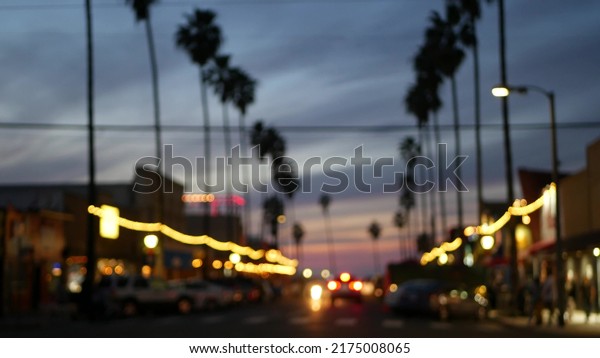Defocused palm trees in Ocean Beach, lights in\
twilight, California coast, San Diego, USA. Row of palmtrees and\
cars on evening road in dusk. Illuminated garlands glowing on\
waterfront city\
street.