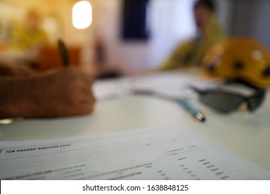 Defocused Personal Protective Equipment Safety Helmet Head Protection Placing On Table Worker Writing Safe Risk Assessment Job Safety Analysis Prior Performing High Risk Paperwork At The Foreground