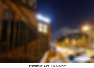 Defocused Photography. Quiet City Street After Snowfall On A Winter Evening. Warm Yellow Street Lighting Against A Blue Night Sky. City Landscape.