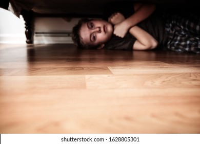 Defocused Scared Boy Hiding Under The Bed, Shallow Focus On Floor In Center Of Image