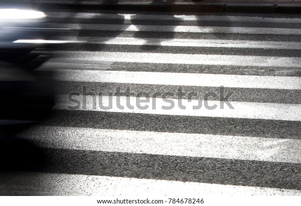 Defocused\
shadows of pedestrians waiting to cross the street on zebra\
crosswalk and driving car ,  in black and\
white