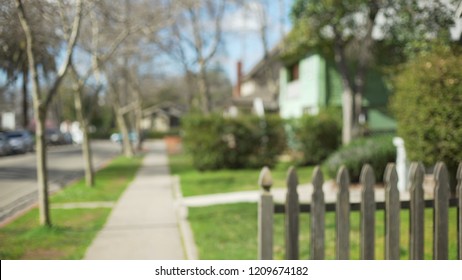 Defocused side view of a typical suburban street and homes behind picket fence