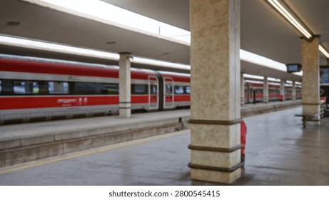 Defocused train platform scene with blurred red carriage, concrete pillars and empty tracks in soft bokeh; background copyspace backplate calm.