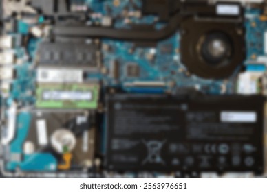 A defocused view of a laptop's internal components. Visible elements include a circuit board, cooling fan, and various electronic parts. 