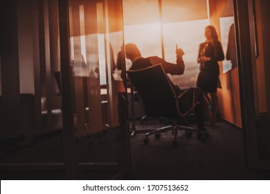 Defocused View Of A Modern Boardroom With A Silhouette Of A Male Boss Tumb Up Praising His Female Subordinate For Her Report For The Successes Achieved In The Current Month; A Window Behind With Flare