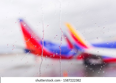 Defocused View On Airplanes Through Passenger Window With Rain Drops. Concept Of Flight Cancellation Or Delay Due To Inclement Weather, Such As Thunderstorm, Hurricane, Or Blizzard