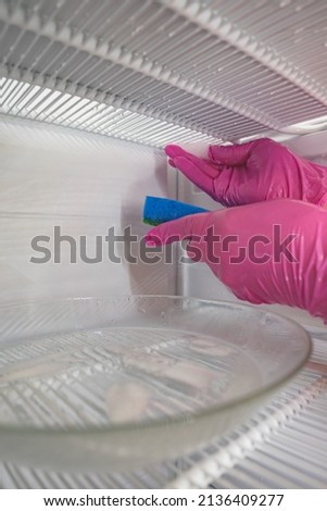 Defrosting and cleaning the freezer. A woman in latex gloves wipes meltwater with a sponge. Shallow depth of field. 