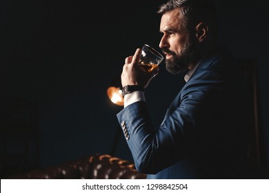 Degustation, tasting. Man with beard holds glass of brandy. Tasting and degustation concept. Bearded businessman in elegant suit with glass of whiskey. Sommelier tastes expensive drink.