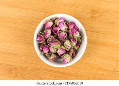 Dehydrated Pink Rose Buds In A White Bowl Top Down View On A Wood Cutting Board