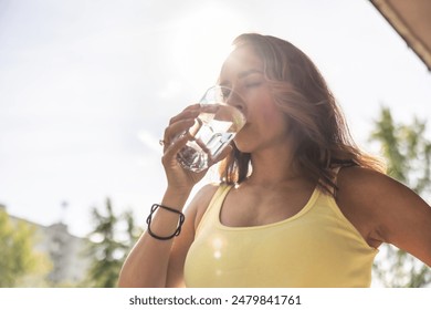 Dehydrated woman drinks clean water from a glass to replenish fluids during hot summer days.