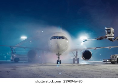 Deicing of airplane before flight. Winter frosty night and ground service at airport during snowfall.
