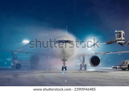 Deicing of airplane before flight. Winter frosty night and ground service at airport during snowfall.
