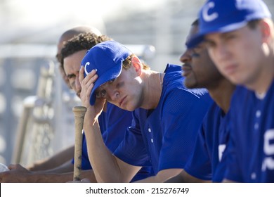 Dejected Baseball Team, In Blue Uniform, Sitting On Bench In Stand During Competitive Baseball Game, Side View (differential Focus)