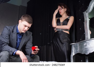 Dejected Young Man Sitting On The End Of The Bed Looking At The Romantic Red Ring Box After His Proposal Of Marriage Is Rejected By His Girlfriend