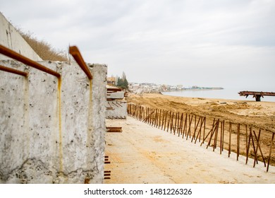 Delayed Sea Wall Construction. Rusty Armature Carcass. Beach And A City On The Background.