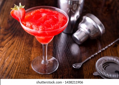 A delcious frozen strawberry daiquiri on a wooden bar counter top.