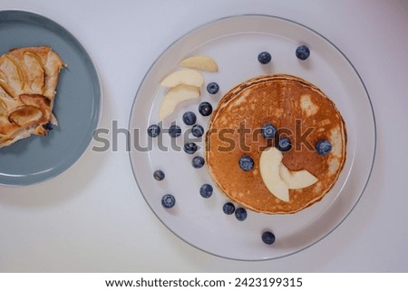 Delectable Delights: Blueberry pancakes with apple slices on a light background, served on a blue and white plate. A mouthwatering treat for any occasion.