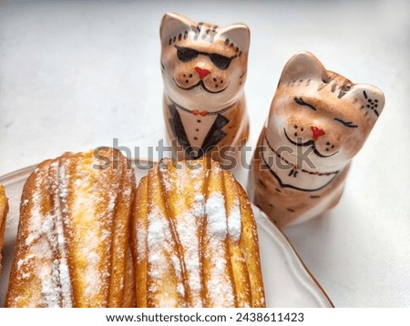 Delectable Dessert Pastries With Charming Porcelain Cat Figurines. Piped cakes sprinkled with sugar beside whimsical cat ornaments
