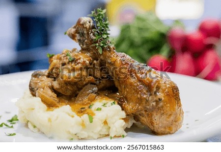 A delectable dish featuring succulent chicken drumsticks smothered in a creamy mushroom sauce, served alongside a generous portion of smooth, buttery mashed potatoes. The rich, savory flavors of the m