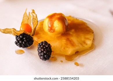 A delectable fruit dessert features pineapple, blackberries, and a physalis on a white plate, creating a delightful and artistic presentation with syrup drizzle. High quality photo