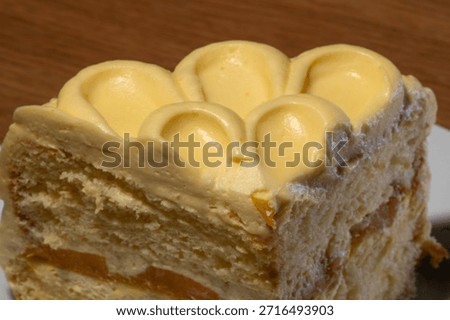 A delectable single slice of cake is presented with decorative yellow cream frosting and visible orange fruit layers on a white plate.