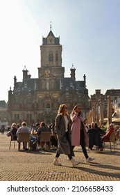 Delft, the Netherlands - October 2021: people sitting on sunny terrace and two girls walking on market square in front of old town hall in dutch city Delft