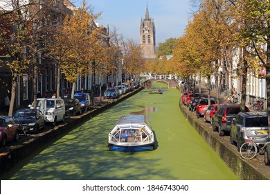 Delft, The Netherlands - October 21, 2016: View of a tourist boat sailing near the tower of the Oude Kerk (Old Church) and  autumnd trees in a canal in Delft, The Netherlands on October 21, 2016