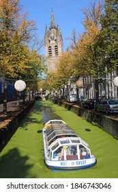 Delft, The Netherlands - October 21, 2016: View of a tourist boat sailing near the tower of the Oude Kerk (Old Church) and trees  in a canal in Delft, The Netherlands on October 21, 2016