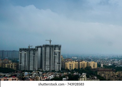 Delhi, India - 3rd Sept'17: Noida Sky Scraper Under Construction In The Middle Of Smaller Buildings. Shot Against A Beautiful Cloudy Sky