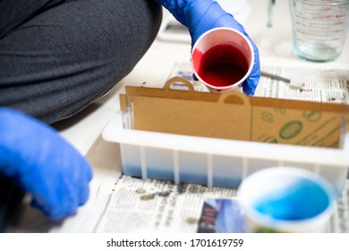 Delhi, India - Circa 2020 : Blue Gloved Hand Pouring Red Liquid From A Paper Cup Into A Mold With Partitions For Making A Home Made Soap For Small Industries Or Even As A Hobby For The Time At Home