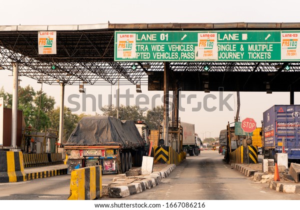 Delhi, India - circa 2020 : Empty toll booth on\
indian highway with FASTag callout on the headboard and traffic\
waiting. This mandatory RFID tag makes cashless digital payment\
necessary on Indian