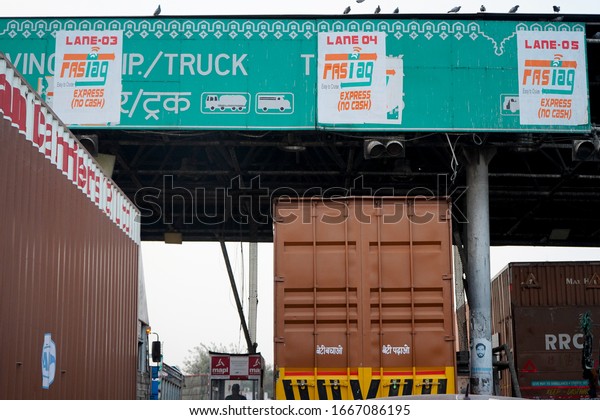 Delhi, India - circa 2020 : Trucks and vehicles\
waiting at an NHAI toll booth with FASTag cashless payment callout.\
Shot form an eye level shows the various trucks and cars passing\
quickly using this