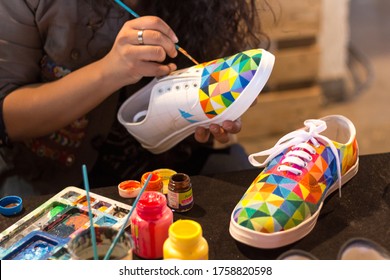 DELHI, INDIA - FEB 2, 2018: A female designer painting a shoe besides other shoes she has already painted for her customers.
