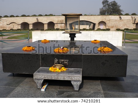 Delhi, India - February 5, 2011: Altar like black marble platform with eternal flame on the spot where Gandhi was cremated at Gandhi Ray Ghat park. Orange flower leis. Beige  and short white wall back