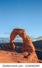 Delicate Arch On A Beautiful Sunny Day With The Moon Overhead At Arches National Park, Utah