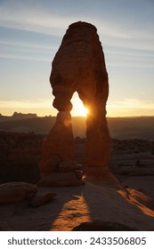 The Delicate Arch at sunset with sun rays peering through its opening, casting a warm glow over the sandstone landmark.