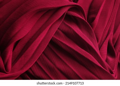 Delicate background texture: elegant red silk pleated fabric. Tissue clothing, crimson luxurious dress textile with folds. Burgundy chiffon cloth, waves 