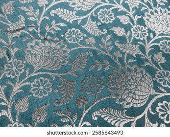 A delicate close-up of golden thread embroidery forms intricate floral patterns on luxurious sky-blue silk damask, shimmering elegantly with every fold. 