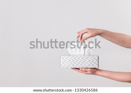 Delicate female hands pulling a tissue out of a gray tissue box.
