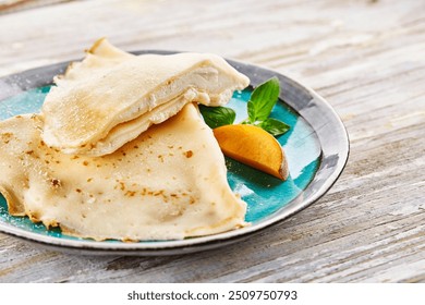 Delicate crêpes filled with cream, drizzled with chocolate sauce and garnished with fresh mint, a peach slice, and blueberries. Served on a black plate with powdered sugar. - Powered by Shutterstock