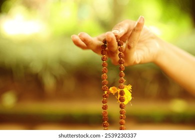 A delicate hand holding prayer beads in a serene garden setting - Powered by Shutterstock