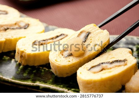 A delicate Korean rolled omelet with eel (jang-eo gyeranmari), served with grated radish and chopsticks.