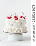 Delicate lambeth style birthday cake with white cream cheese frosting decorated with cocktail cherries on the white background