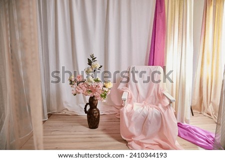 Delicate pink bright interior of the room with an armchair, vase with roses, draped curtains and a window. Location and background in the photo studio